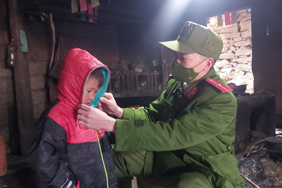 Thiếu úy Hoàng Minh Sơn, công an xã Xín Cái mặc áo ấm cho cháu Già Mí Dính, thôn Lùng Thũng, xã Xín Cái, huyện Mèo Vạc (Hà Giang). (Ảnh: Nguyễn Chiến/TTXVN)