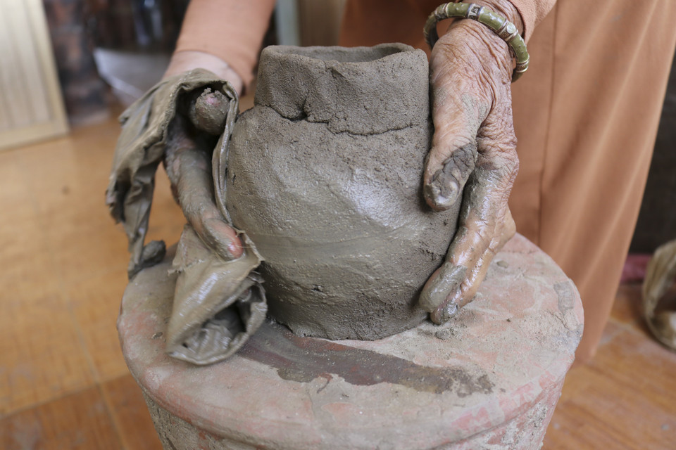 Người thợ không sử dụng bàn xoay mà dùng bàn chân xoay quanh một chiếc trụ cố định rồi nặn, nắn, miết để biến cục đất sét thành sản phẩm gốm theo ý muốn. (Ảnh: Nguyễn Thành/TTXVN)