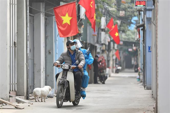 Hình ảnh thành viên Tổ hỗ trợ theo dõi người nhiễm COVID-19 tại nhà phường Lĩnh Nam được trang bị đồ bảo hộ, chở oxy bằng xe máy đến tận nhà người bệnh. (Ảnh: Minh Quyết/TTXVN)