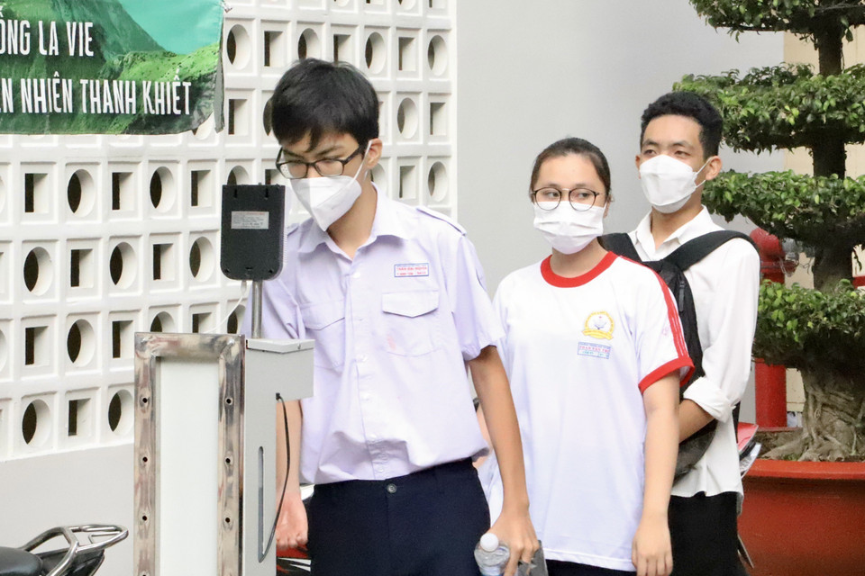 Các thí sinh kiểm tra thân nhiệt khi đến dự thi tại điểm thi trường Trung học phổ thông Bùi Thị Xuân (Quận 1). (Ảnh: Hồng Giang/TTXVN)