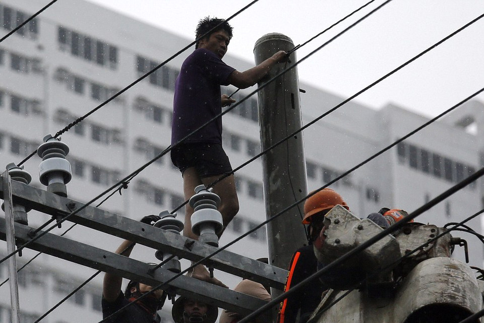 Một nghi phạm do quá sợ hãi mà leo lên cột điện, các nhân viên cứu hộ đang thuyết phục hắn leo xuống. (Nguồn: Dailymail)