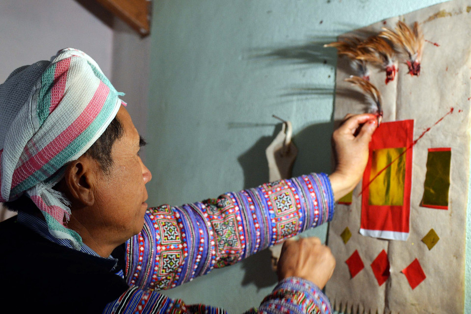  Cắt tiết gà xong, thầy cúng nhổ năm nhúm lông gà nhúng tiết để đính lên ban thờ vừa được thay mới. (Ảnh: Thanh Hà/TTXVN) 