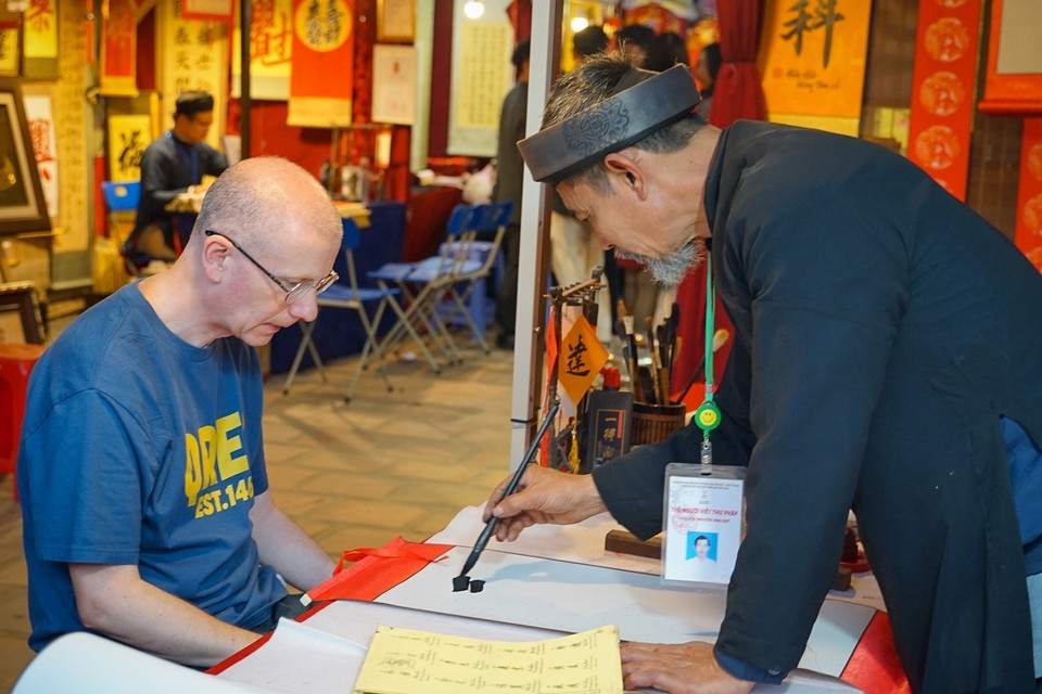 Một du khách nước ngoài chăm chú từng nét bút của ông đồ tại Hội chữ Xuân Quý Mão 2023. (Ảnh: Khánh Hòa/TTXVN)