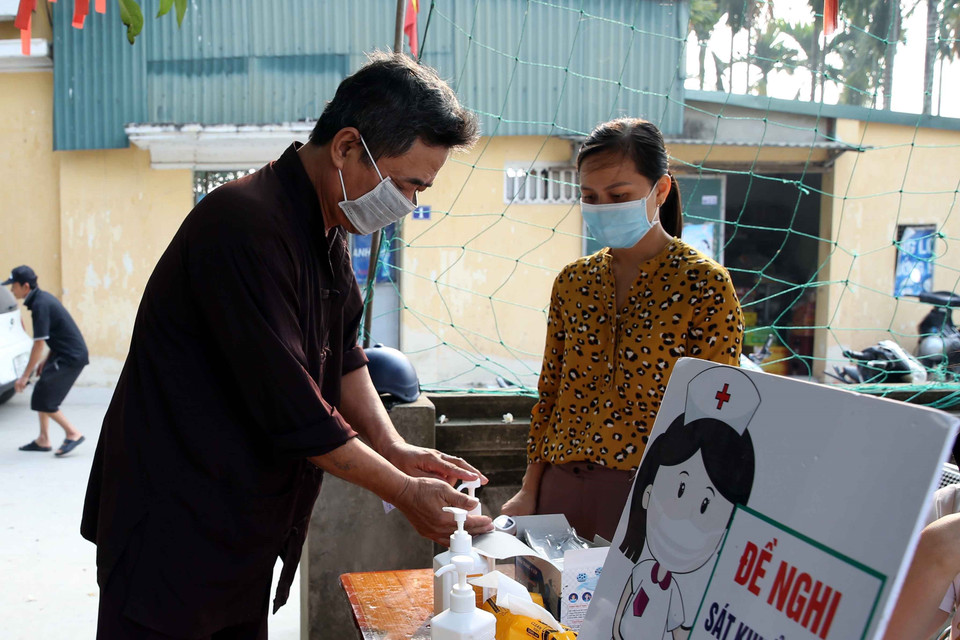 Cử tri sát khuẩn tay phòng, chống dịch COVID-19 trước khi vào bỏ phiếu bầu cử tại điểm bầu cử số 04, thôn Đào Xá, xã Hoàng Long, huyện Phú Xuyên, Hà Nội. (Ảnh: Phạm Kiên/TTXVN)