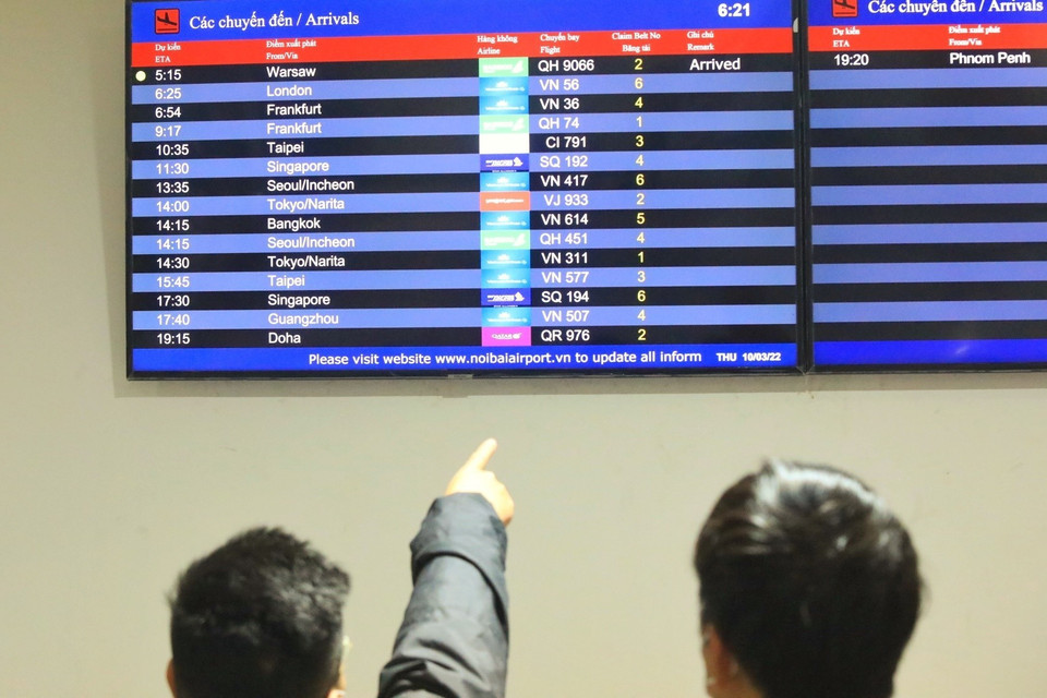 Người thân dõi theo bảng điện tử cập nhật chuyến bay về từ Ba Lan. (Ảnh: Tuấn Anh/TTXVN)