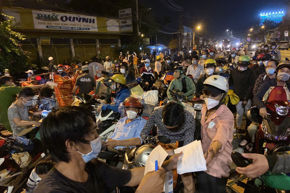 Lực lượng chức năng hướng dẫn người dân ghi phiếu thông tin chốt kiểm soát khu vực cửa ngõ trên Quốc lộ 1A, giáp ranh giữa Thành phố Hồ Chí Minh và tỉnh Long An trong đêm 30/9. (Ảnh: Mạnh Linh/TTXVN)