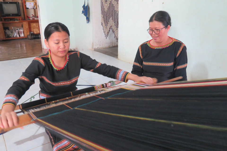 Em Rơ Manh Minh Thư (sinh năm 2006, con gái của nghệ nhân Y Thúy) đang được mẹ truyền dạy nghề dệt thổ cẩm. (Ảnh: Dư Toán/TTXVN)