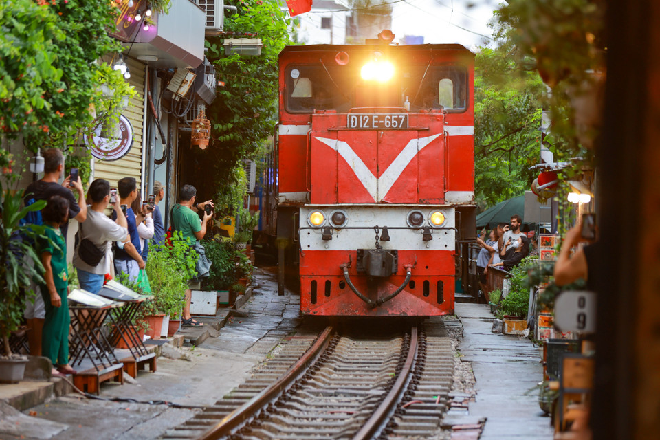 Du khách đứng néo vào hai bên đường, lấy điện thoại để ghi lại khoảnh khắc khi tàu lướt nhanh qua các quán càphê. (Ảnh: Minh Sơn/Vietnam+)