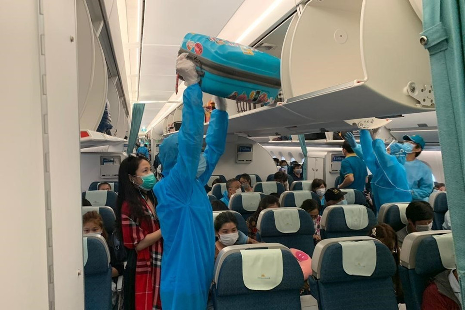 Các tiếp viên Vietnam Airlines trong bộ đồ bảo hộ y tế hỗ trợ hành khách xếp hành lý trên tàu bay, trước khi khởi hành về nước. (Ảnh: Hà Ngọc/TTXVN)