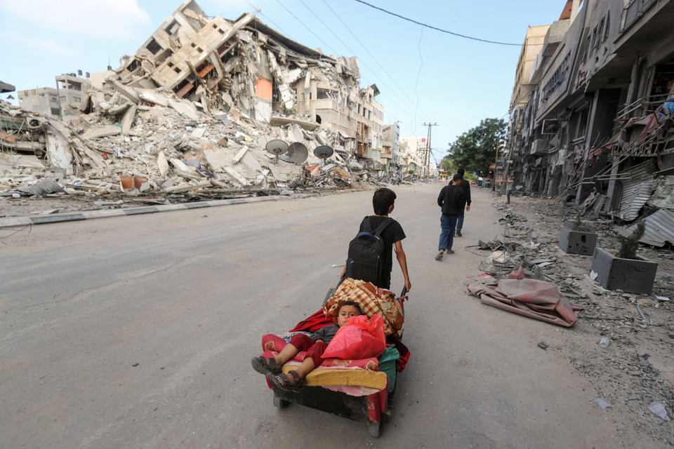 Một cậu bé người Palestine kéo xe chở em trai và đồ đạc, chạy trốn khỏi nhà trong các cuộc tấn công bằng không quân và pháo binh của Israel. (Ảnh: Reuters)