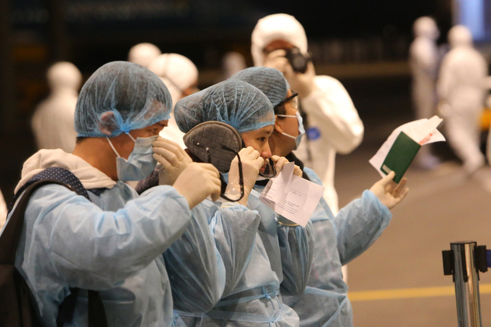 Công dân Việt Nam trở về từ Vũ Hán (Trung Quốc) được trang bị đồ bảo hộ và hướng dẫn làm thủ tục nhập cảnh tại sân bay Vân Đồn.(Ảnh: Dương Giang/TTXVN)