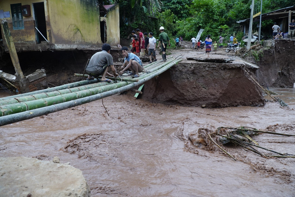 Người dân làm cầu tạm để đi sau khi bị nước lũ cuốn trôi mất đường. (Ảnh: Xuân Tư/TTXVN)