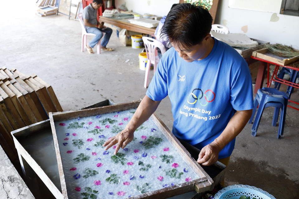 Nghệ nhân Nalongkone Khounphachansi, chủ cơ sở làm giấy Saa tại bản Xienglek, tỉnh Luang Prabang, trang trí hoa lá lên khuôn giấy. (Ảnh: Phạm Kiên/TTXVN)
