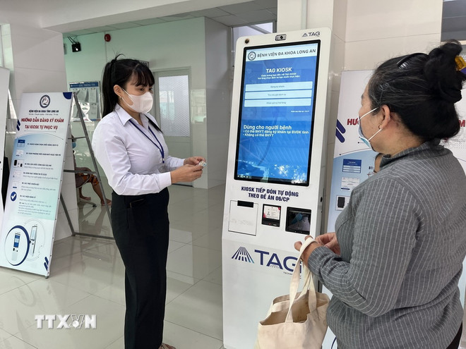 Nhân viên Bệnh viện Đa khoa Long An giúp người dân lấy số thứ tự trên kiốt đăng ký khám chữa bệnh tự động. (Ảnh: Đức Hạnh/TTXVN) ttxvn-kiot-sih-trac-hoc.jpg