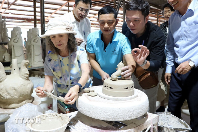 Các vị khách quốc tế trải nghiệm vẽ hoa văn lên các bình gốm thô. (Ảnh: Mạnh Tú/TTXVN)