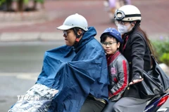 Một gia đình ra đường trong chiếc áo mưa khi trời có mưa phùn. (Ảnh: Thanh Tùng/TTXVN)