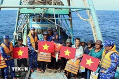 Lực lượng chức năng tặng cờ Tổ quốc, áo phao cho ngư dân trên biển. (Ảnh: TTXVN phát)