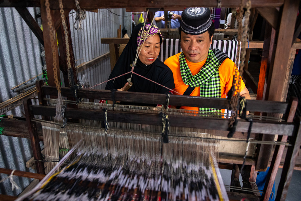 Du khách hào hứng trải nghiệm nghề dệt thổ cẩm tại gia đình ông Mohamad ở ấp Phũm Soài, xã Châu Phong, thị xã Tân Châu, tỉnh An Giang. (Ảnh: Hoài Nam/Vietnam+)