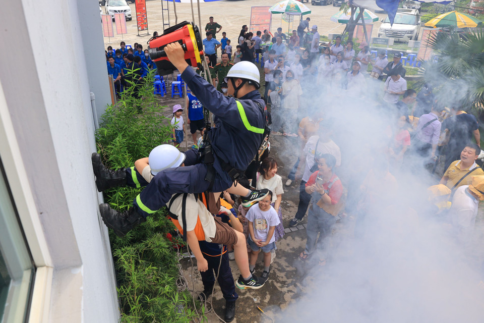 Em nhỏ tham gia trải nghiệm thoát hiểm bằng thang dây cùng chú lính cứu hoả. (Ảnh: Hoài Nam/Vietnam+)