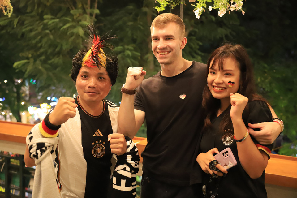 Kevin (người Đức ở giữa) thấy rất bất ngờ khi có rất nhiều người Việt Nam yêu thích đội tuyển Đức như vậy. Anh chia sẻ: ‘Tôi dự đoán hôm nay tuyển Đức thắng 2-0 trước Nhật Bản và tiến vào vòng cuối.’ (Ảnh: PV/Vietnam+)