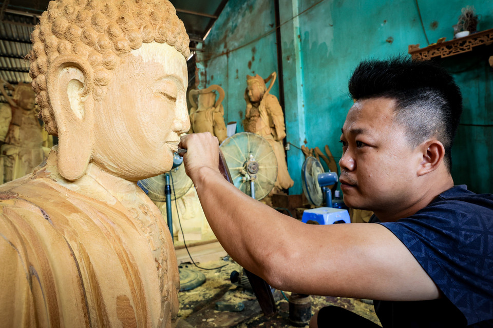 Anh Nguyễn Đăng Đại, con trai nghệ nhân Nguyễn Đăng Hạc, đã gắn bó với 'bản nhạc' làng nghề hơn 20 năm, từ ngày còn tấm bé anh đã quen với tiếng đục đẽo lách cách. (Ảnh: Hoài Nam/Vietnam+)