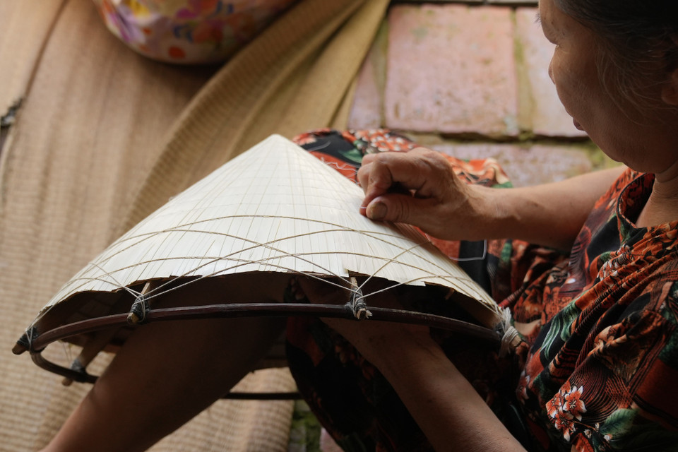 Tiếp theo, người thợ xếp từng lá vào vòng nón, một lớp mo tre và một lớp lá nữa rồi người làm nón sẽ khâu lại. Đây là một công đoạn rất khó bởi lá rất dễ rách nếu không có sự khéo léo. (Ảnh: Hoài Nam/Vietnam+)