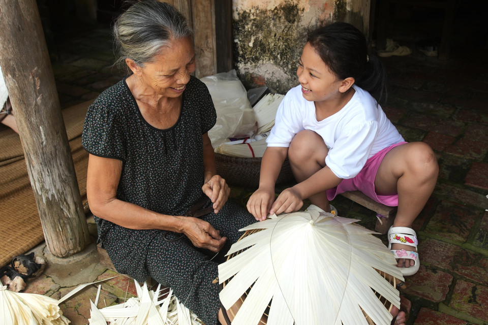 Người già truyền lại cho lớp trẻ, người lớn dạy cho trẻ nhỏ, cứ thế mà nghề nối nghề, họ vững tin và âm thầm gìn giữ mãi chiếc nón lá truyền thống, vừa bảo tồn nét văn hóa của người Việt. (Ảnh: Hoài Nam/Vietnam+)
