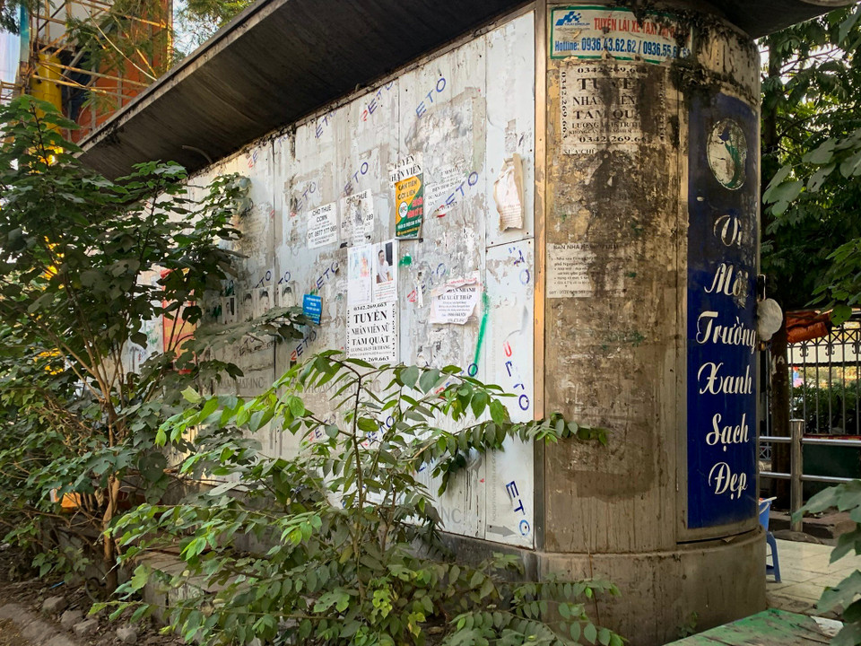 Nhà vệ sinh công cộng trên đường Nguyễn Hoàng (Nam Từ Liêm, Hà Nội) trong cảnh hoang tàn, cỏ cây mọc um tùm và mang trên mình chi chít những tờ quảng cáo. (Ảnh: Hoài Nam/Vietnam+)