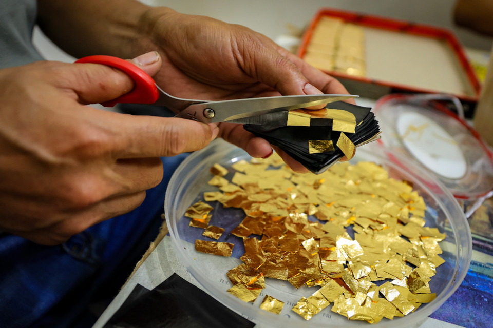 Các công đoạn cắt dòng' và 'sang vàng' tại gia đình nghệ nhân Nguyễn Văn Hiệp. Đây là công đoạn phải làm trong phòng kín, không được dùng quạt vì vàng sau khi quỳ rất mỏng, chỉ cần gió nhẹ cũng có thể làm bay những lá vàng. (Ảnh: Hoài Nam/Vietnam+)