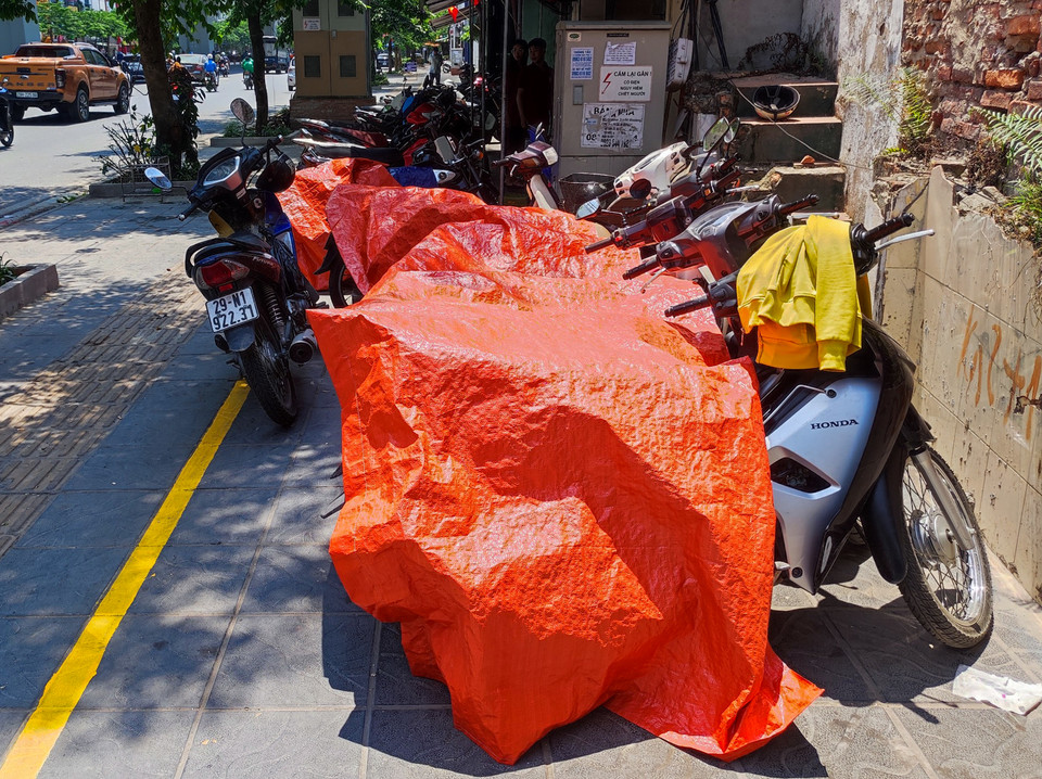 Người dân dùng bạt để che phủ phương tiện dưới thời thiết nắng nóng gay gắt. (Ảnh: Hoài Nam/Vietnam+)