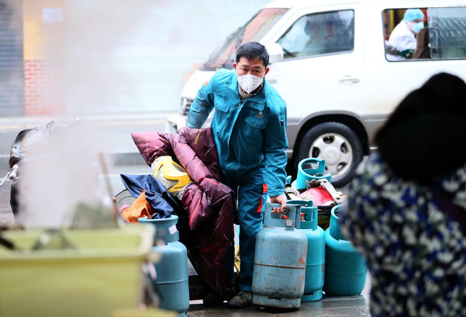 Nhân viên giao gas cho một nhà hàng ở Vũ Hán, phía sau là hình ảnh xe cứu thương (Ảnh: Chinadaily)