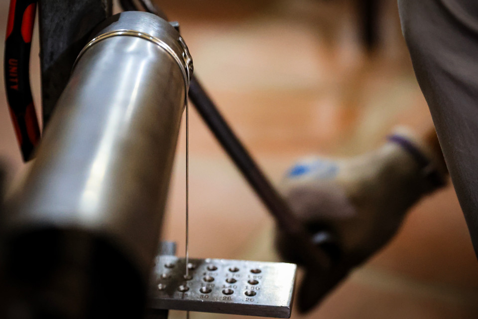 Chia sẻ về đất nghề được mệnh danh là 'tứ nghệ tinh' trên đất Thăng Long xưa, nghệ nhân Tuấn Anh nói về sự tỉ mỉ, kỳ công trong từng công đoạn. Để làm ra một sản phẩm đậu bạc hoàn chỉnh, sau khi nấu rồi đúc thành các thanh bạc, đưa qua máy cán, cán thành các sợi bạc nhỏ hơn, rồi đưa vào bàn kép có các lỗ từ to đến nhỏ để tạo ra sợi nhỏ như sợi chỉ khâu. (Ảnh: Hoài Nam/Vietnam+)