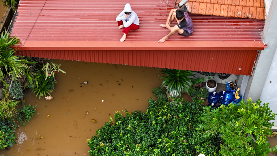 Người dân ngồi trên nóc nhà khi nước dâng lên nhanh. (Ảnh: Hoài Nam/Vietnam+)