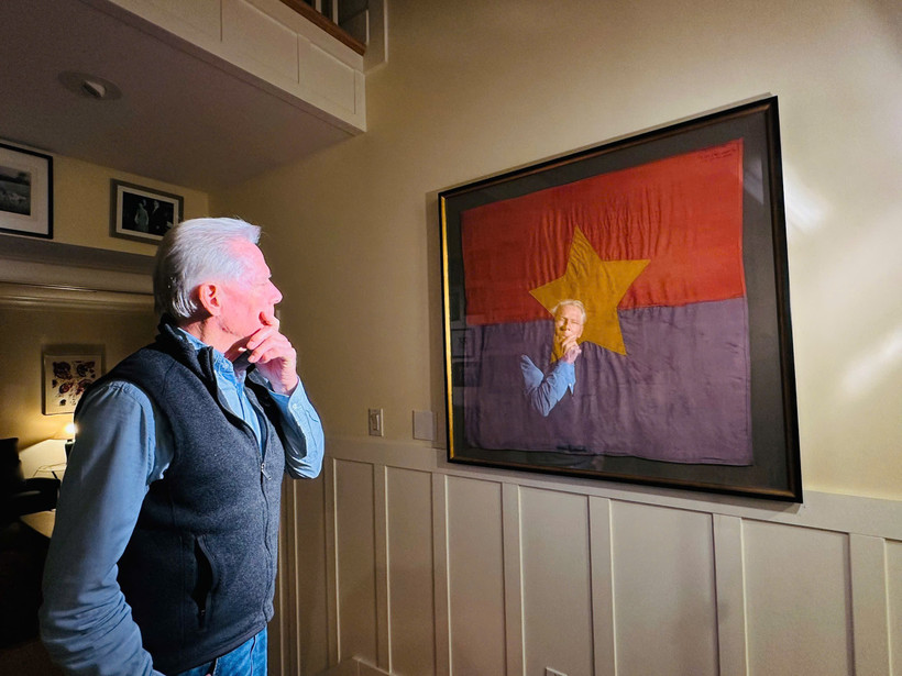 Ông Craig McNamara và lá cờ của Mặt trận dân tộc Giải phóng miền Nam Việt Nam treo tại nhà suốt 60 năm. (Ảnh: VTV)