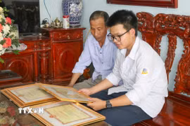 Em Trần Xuân Đam và bố giới thiệu những tấm bằng khen đã đạt được trong quá trình học tập. (Ảnh: Công Luật/TTXVN)