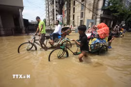 Một em nhỏ cùng những người lớn trong dòng nước lũ ở Sylhet, Bangladesh, ngày 19/5/2022. (Ảnh: AFP/TTXVN)