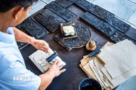 Từ các bản mộc đã khắc họa tiết, người thợ dùng mực đen được làm từ tro rơm rạ và lá bạc để in đều lên bề mặt tranh. (Ảnh: Vân Chi/TTXVN phát)