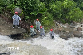 Lực lượng chức năng căng dây để trục vớt thi thể người đàn ông dưới dòng nước chảy siết. (Ảnh: TTXVN phát)