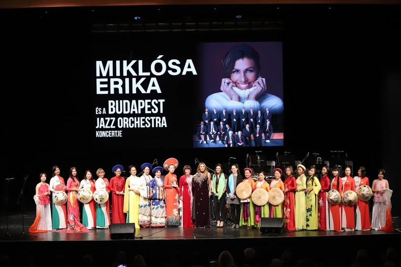 Tiến sỹ Phan Bích Thiện (áo dài đỏ đứng giữa), Chủ tịch Hội Phụ nữ Việt Nam tại Hungary, đã thay mặt cộng đồng người Việt trao tặng nghệ sỹ Miklósa Erika một bộ áo dài Việt Nam được nghệ nhân Việt Nam may thủ công tinh xảo. Món quà đầy ý nghĩa vừa tôn vinh văn hóa Việt và biểu trưng cho tình hữu nghị giữa nhân dân hai nước Việt Nam-Hungary (Ảnh: TTXVN )