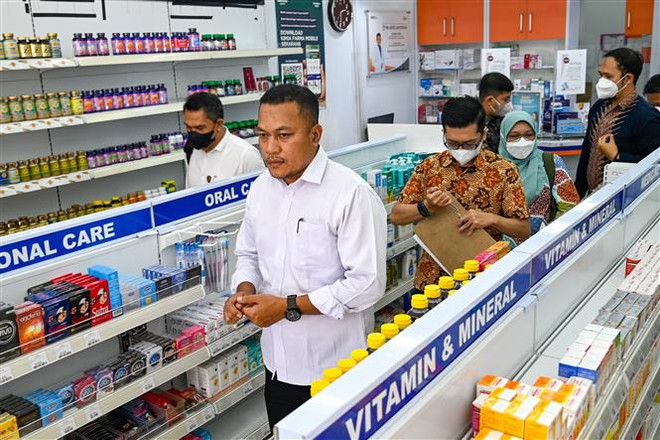 Cảnh sát và nhân viên y tế kiểm tra thuốc siro ho tại một cửa hàng thuốc ở Banda Aceh (Indonesia), ngày 24/10/2022. (Ảnh: AFP/TTXVN) Indonesia điều tra cơ quan cấp phép siro ho gây suy thận ở trẻ em ảnh 1