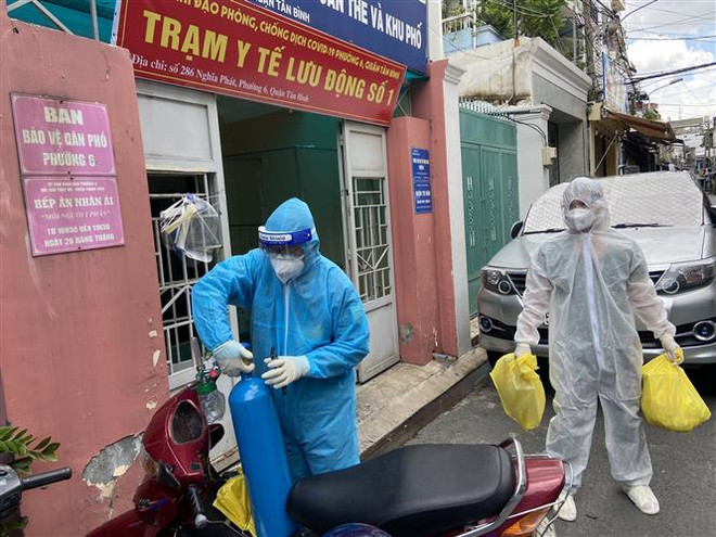 Lực lượng Quân y tại Trạm y tế lưu động số 1 (Phường 6, quận Tân Bình) mang các đồ dùng cần thiết (bình oxy, máy đo nồng độ oxy, ống nghe, nhiệt kế, dung dịch sát khuẩn, khẩu trang…) để đến nhà F0. (Ảnh: Mạnh Linh/TTXVN) Số ca dương tính tăng cao, TP.HCM tăng cường các biện pháp phòng dịch ảnh 1