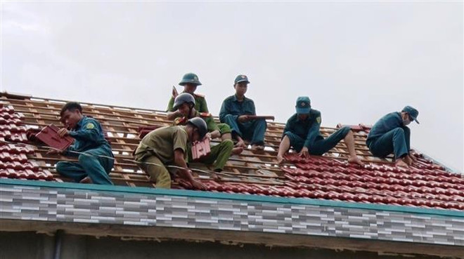 Lực lượng Công an, dân quân huyện Đồng Xuân, Phú Yên hỗ trợ người dân xã vùng sâu Phú Mỡ lợp lại mái nhà. (Ảnh: TTXVN phát) Bão số 9: Các địa phương nỗ lực sửa chữa sự cố điện, đường giao thông ảnh 2