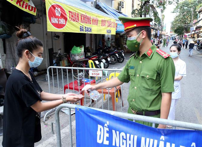 Người dân vào mua đồ thiết yếu tại chợ Đồng Xuân được lực lượng chức năng yêu cầu rửa tay sát khuẩn ngày 24/7/2021. (Ảnh: Phạm Kiên/TTXVN) Hóa giải thách thức, chung sức đồng lòng vì một Việt Nam phát triển ảnh 1