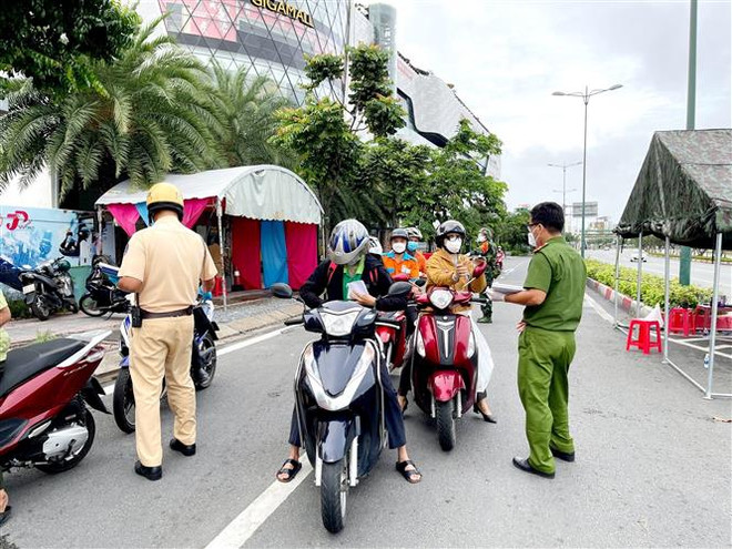 Lực lượng Công an tại chốt kiểm trên đường Phạm Văn Đồng (phường Hiệp Bình Chánh, Thủ Đức) kiểm tra giấy tờ của người lưu thông. (Ảnh: Thành Chung/TTXVN) TP.HCM bổ sung thêm các trường hợp không cần giấy đi đường ảnh 1
