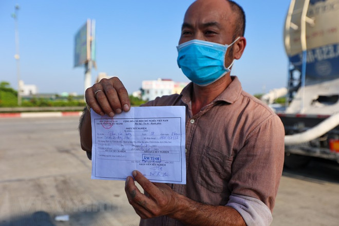 Một tài xế trình giấy xét nghiệm COVID-19 âm tính mới được phép lưu thông qua chốt kiểm soát dịch để vào thành phố. (Ảnh: Minh Sơn/Vietnam+) Bộ GTVT kiến nghị kéo dài hiệu lực giấy xét nghiệm COVID cho lái xe ảnh 1