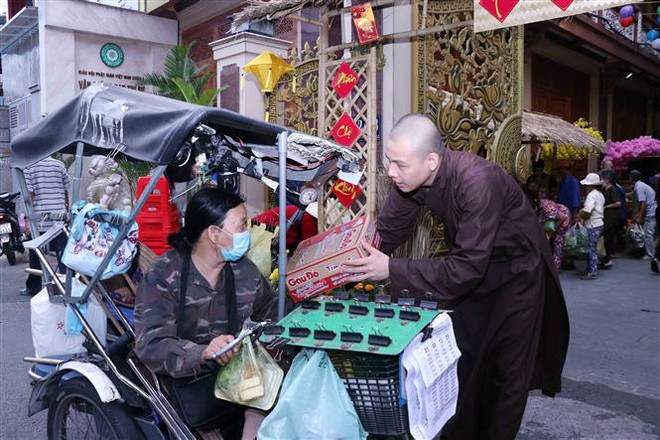 Đại đức Thích Minh Ân, trụ trì chùa Minh Đạo tặng quà Tết cho người bán vé số. (Ảnh: Xuân Khu/TTXVN) Ấm lòng những hoạt động hỗ trợ người nghèo dịp Tết Nguyên đán ảnh 3