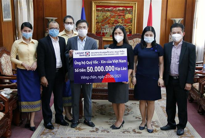 Ông Nguyễn Đức Vũ (Trái) Tổng Giám đốc Ngân hàng Liên doanh Lào - Việt đang trao tượng trưng số tiền 50.000.000 kip (Khoảng 115 triệu đồng) ủng hộ Quỹ vaccine phòng chống COVID-19 của Việt Nam cho Công sứ Trịnh Minh Tâm. (Ảnh: Phạm Kiên/TTXVN) Người Việt tại Lào ủng hộ cuộc chiến chống COVID-19 tại quê nhà ảnh 1