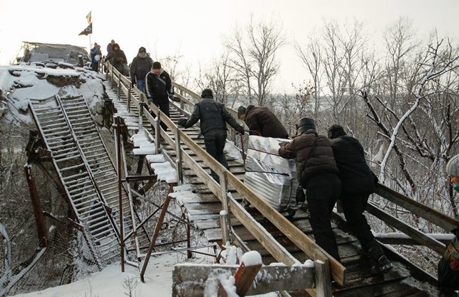 Người dân đi qua chốt kiểm soát giữa quân đội Ukraine và lực lượng đòi độc lập bằng chiếc thang gỗ thay thế cho chiếc cầu bị phá hủy trong một đợt giao tranh ở khu vực Luhansk ngày 16/12. (Nguồn: EPA/TTXVN) NATO hối Nga yêu cầu phe nổi dậy ở Đông Ukraine thực thi ngừng bắn ảnh 1