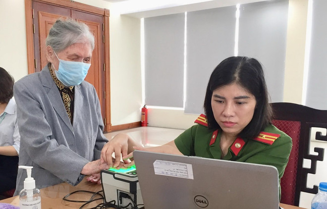 Cán bộ Đội 2, Phòng Cảnh sát quản lý hành chính về trật tự xã hội (Công an thành phố Hà Nội) tận tình phục vụ người dân đến làm thẻ căn cước công dân gắn chíp. (Ảnh: Nguyễn Thắng/TTXVN) Hà Nội: Cao điểm 30 ngày đêm nhận hồ sơ cấp căn cước công dân gắn chíp ảnh 1