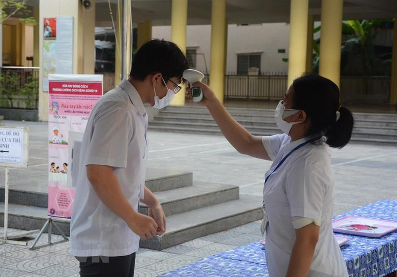 Thí sinh được đo thân nhiệt, rửa tay bằng nước sát khuẩn, thay khẩu trang mới tại cổng điểm thi. (Ảnh: Văn Dũng/TTXVN)